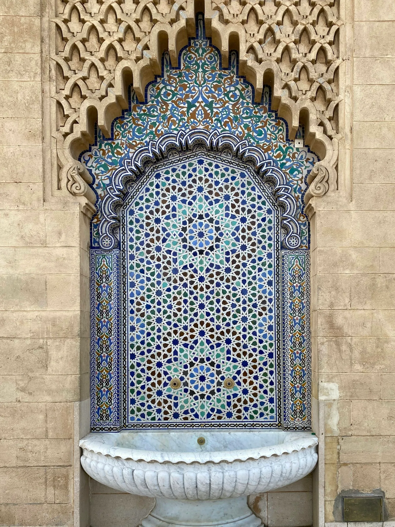 Fontaine en zellige : mosaïque géométrique bleue, verte et blanche sous un arc sculpté